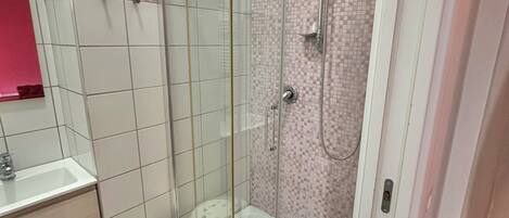 Un baño moderno con ducha acristalada, lavamanos blanco y un pequeño taburete.