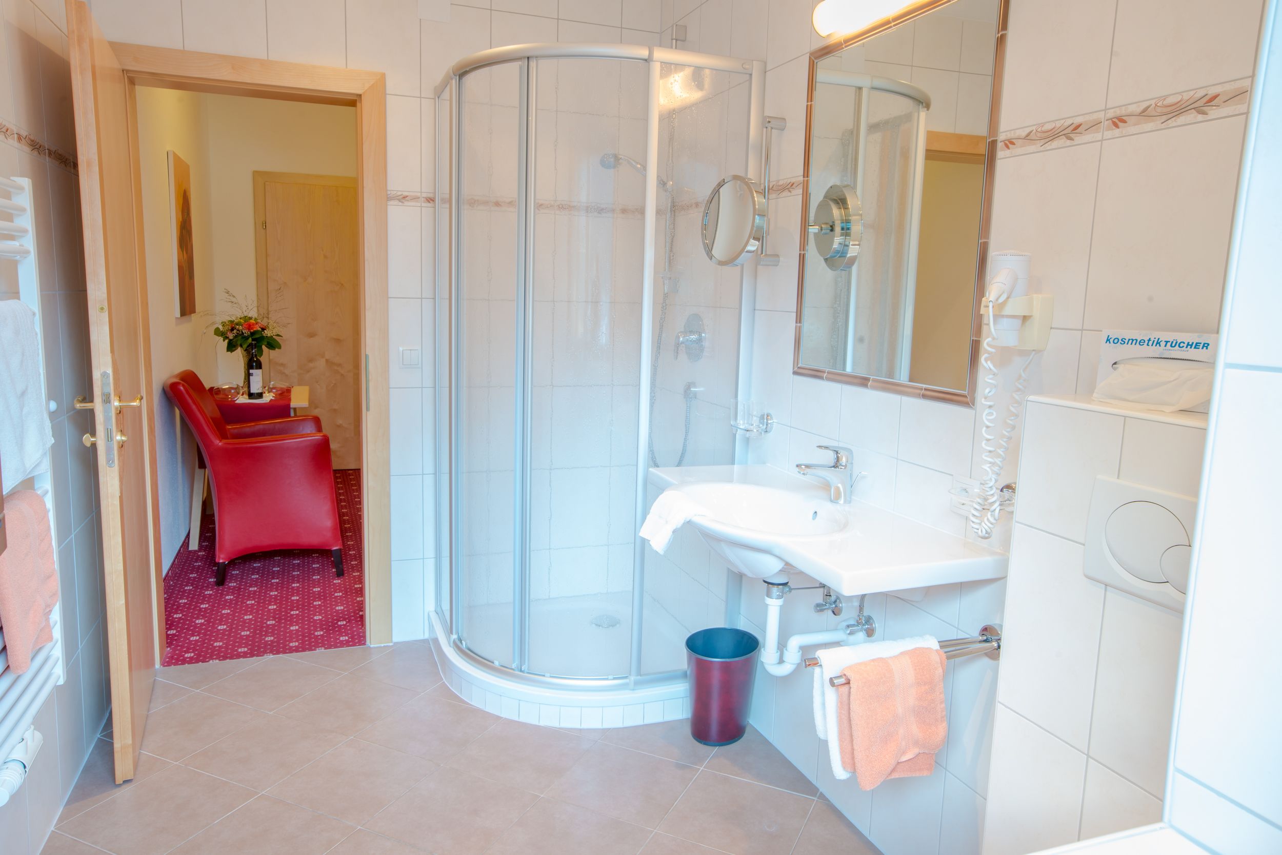 Un baño moderno con ducha de vidrio, un lavabo blanco y una silla roja.