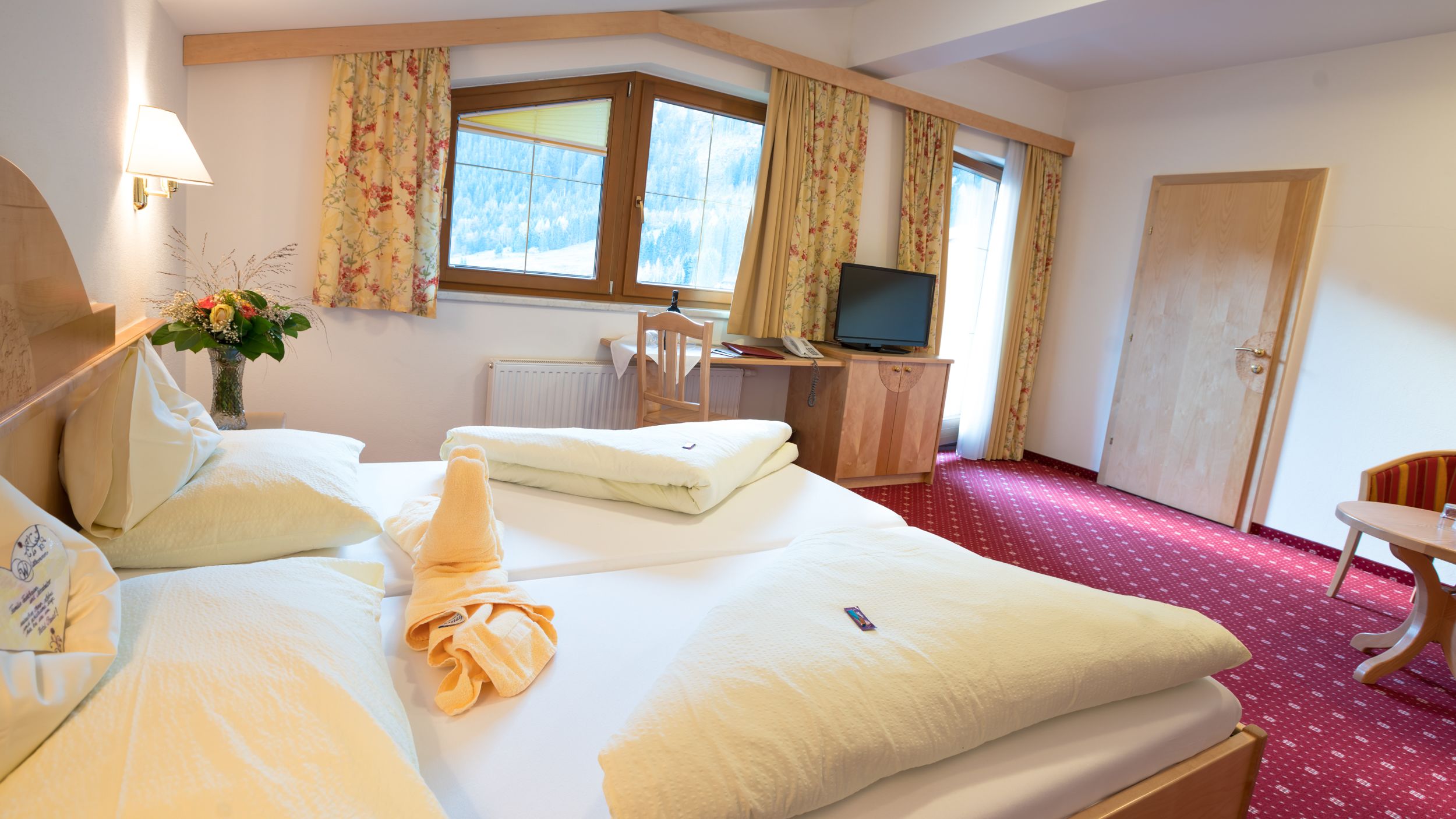 Una habitación de hotel con una cama, un escritorio, un televisor y una ventana con cortinas.