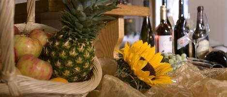A wicker basket with apples and a pineapple, a sunflower, and several wine bottles on a table.