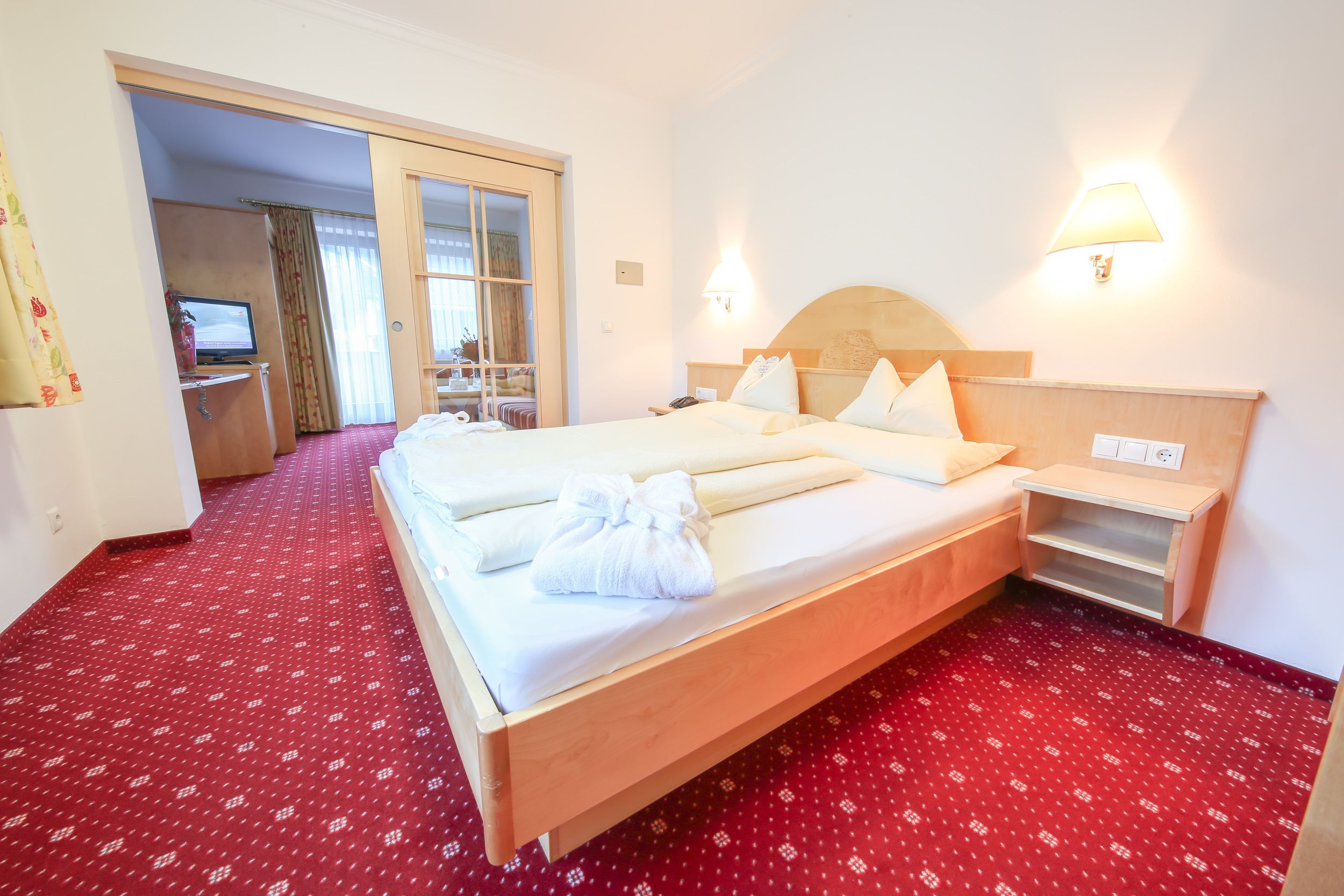 Habitación de hotel con una cama grande, un escritorio con computadora y piso cubierto de alfombra roja.