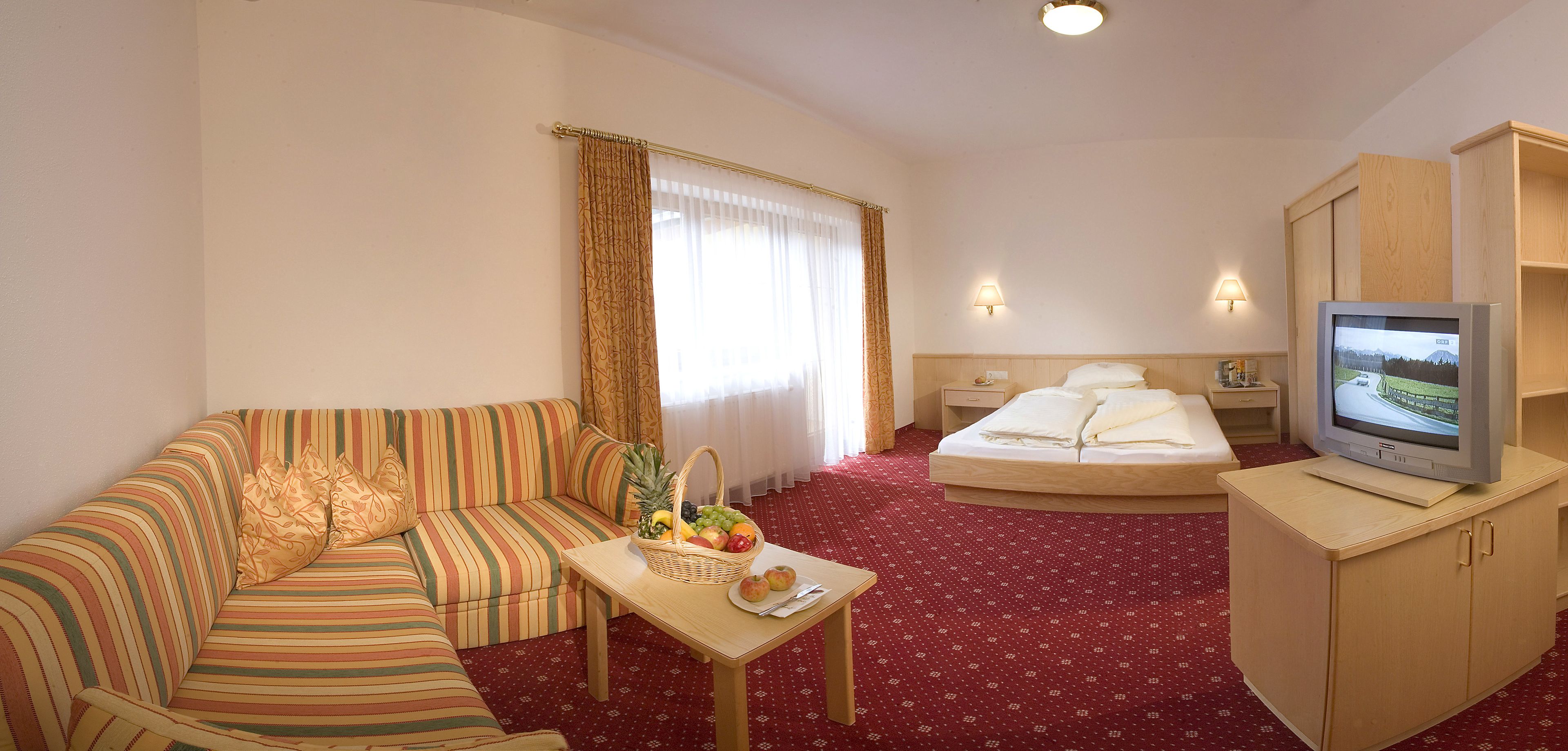 Ein Hotelzimmer mit einem gestreiften Sofa, einem kleinen Tisch mit Obst, einem Bett, einem Fernseher und einem Holzschrank.