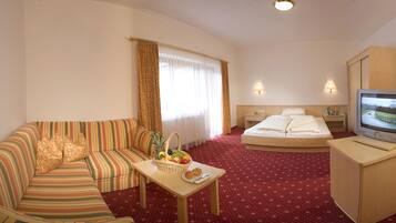 Ein Hotelzimmer mit einem gestreiften Sofa, einem kleinen Tisch mit Obst, einem Bett, einem Fernseher und einem Holzschrank.