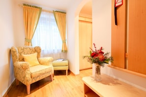 A room with a patterned armchair, a small table with a vase of flowers, and a window with curtains. - Hotel Persal (Finkenberg)