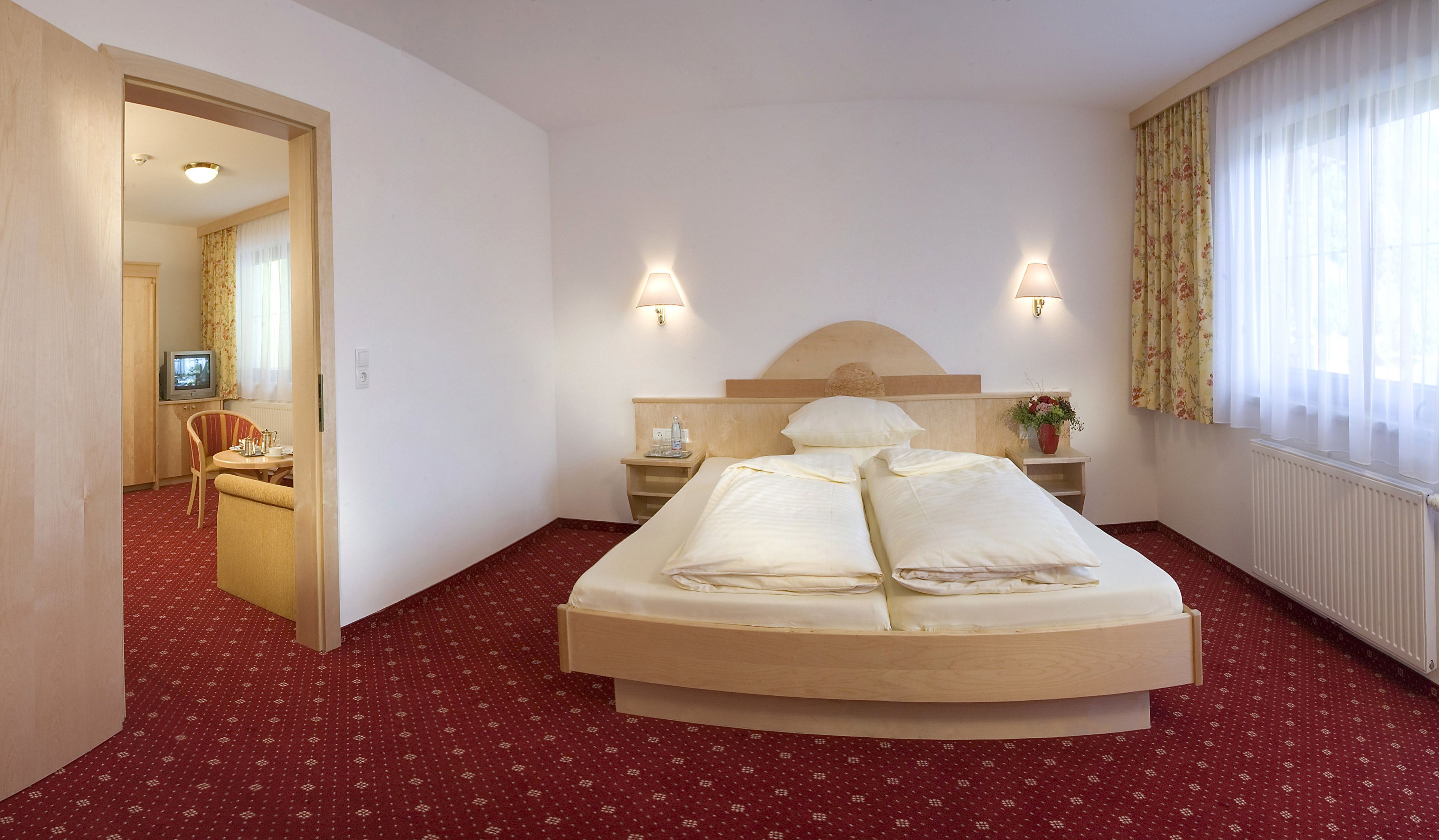 A hotel room with a large bed, two bedside lamps, a TV, a small table, and a chair.