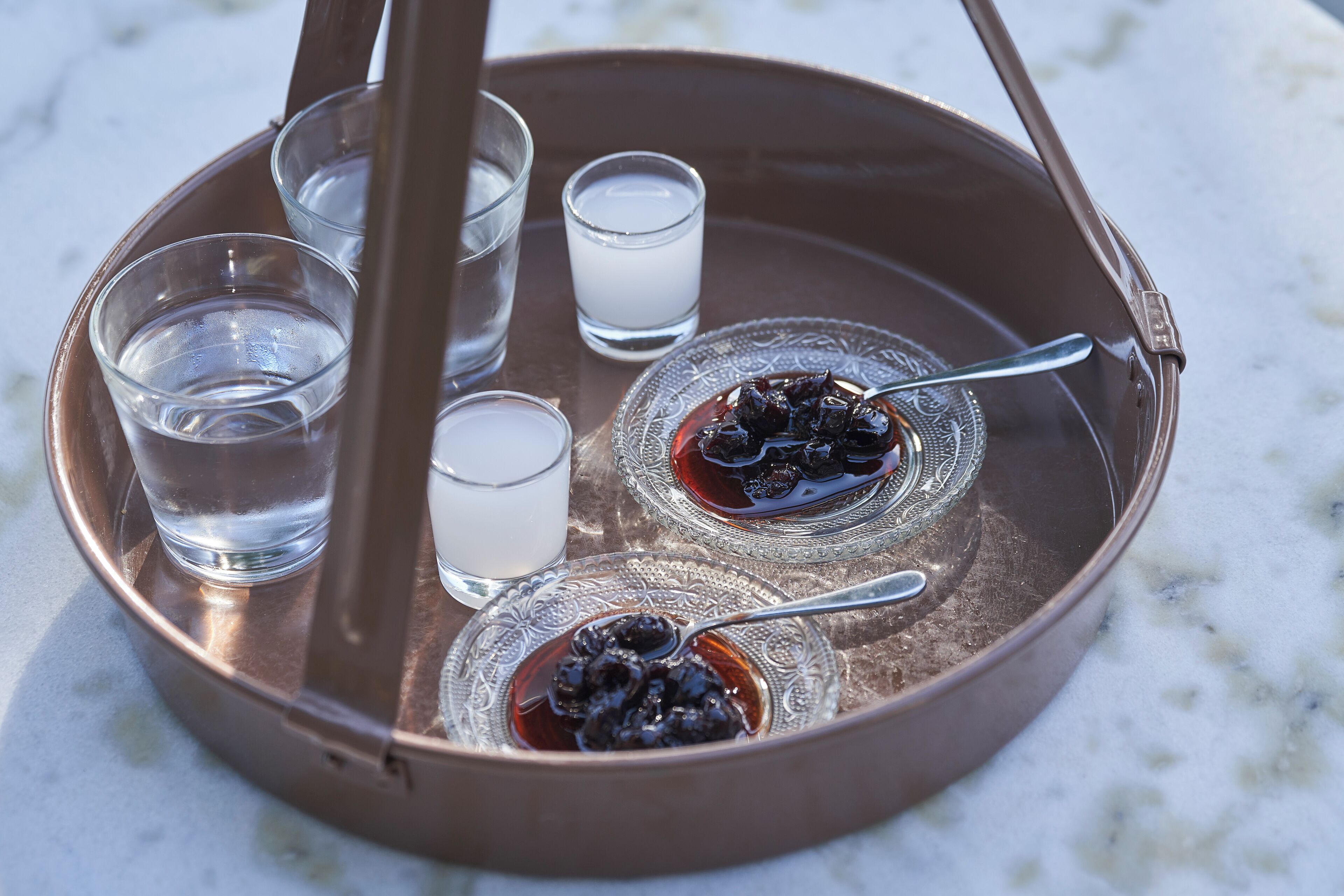 A tray with four glasses of water and two bowls of dark syrup with a spoon.