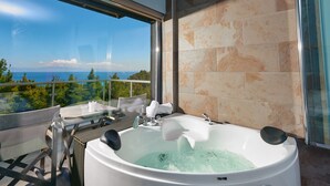 Un baño moderno con una bañera grande, un box de ducha de vidrio y un balcón con vistas al mar.