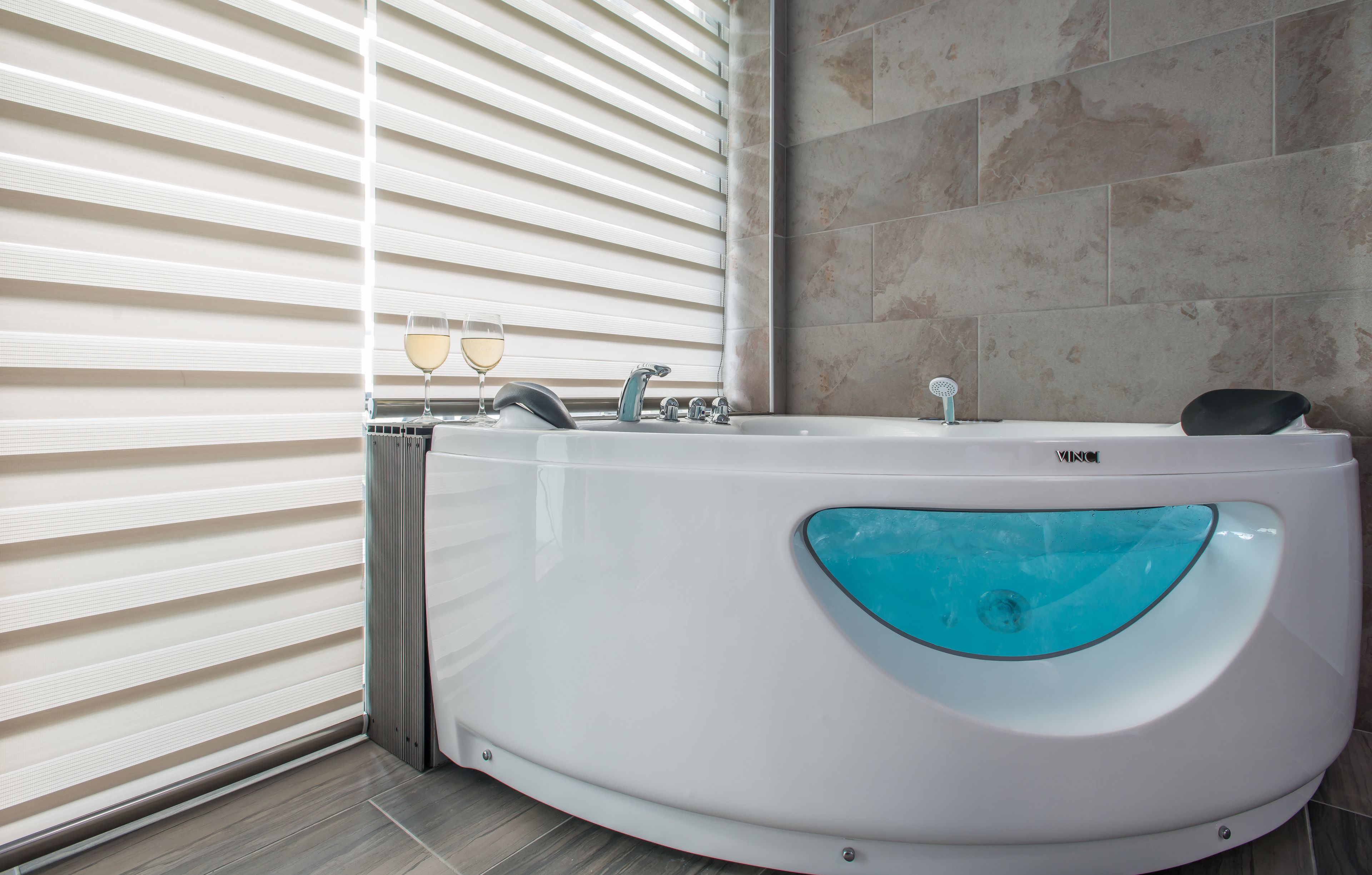 Een moderne badkamer met een vrijstaand bad, een douche met glazen wanden en een groot raam met zonwering.