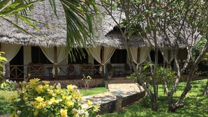 A thatched-roof building with multiple rooms, a stone pathway, and lush greenery. - Kenga Giama Resort (Malindi)