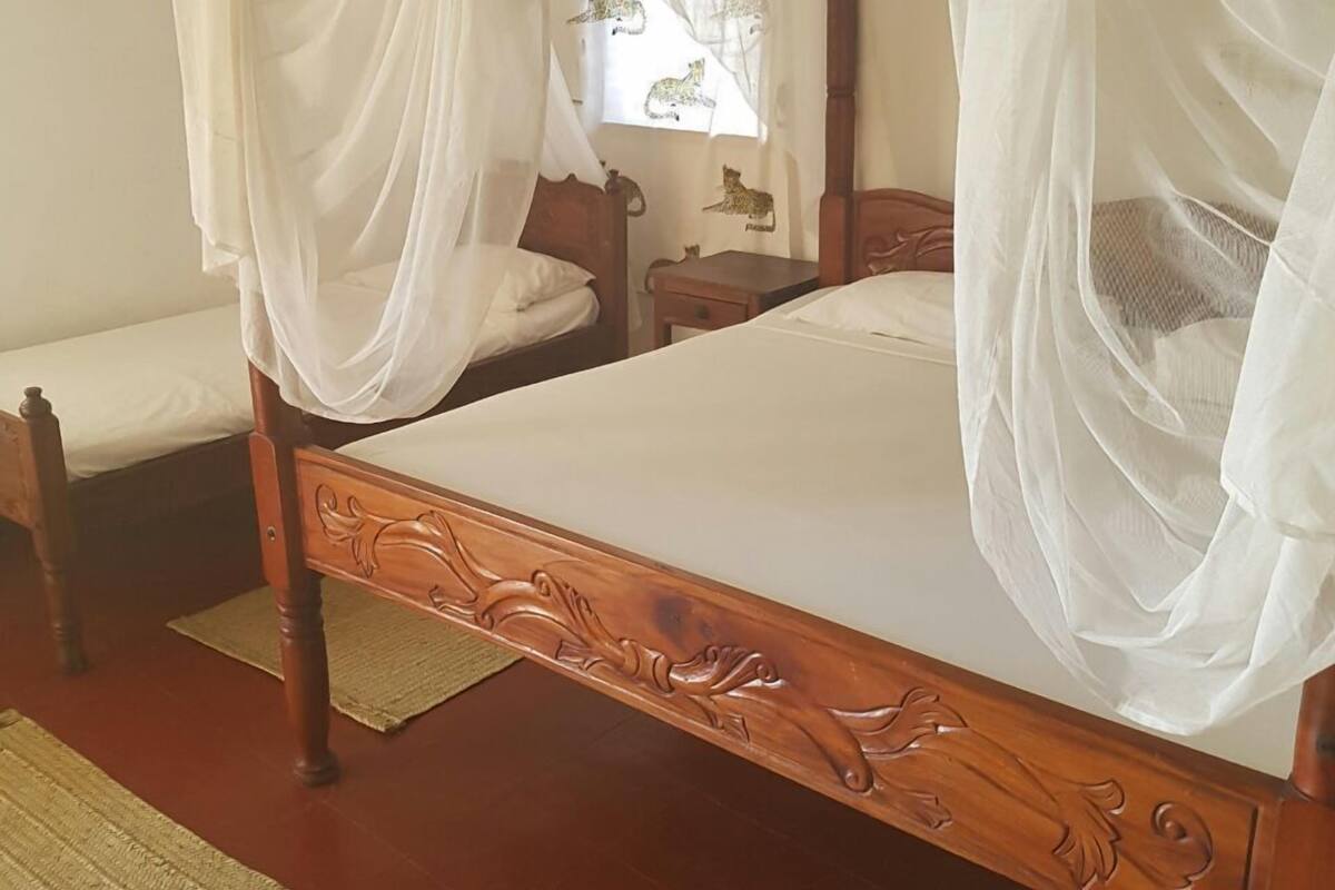 Un lit à baldaquin à quatre poteaux, avec une structure en bois et des détails sculptés, une table de chevet et une chaise.