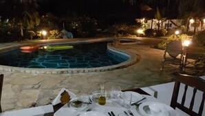 An outdoor dining area with a pool, stone flooring, and tropical plants. - Kenga Giama Resort (Malindi)