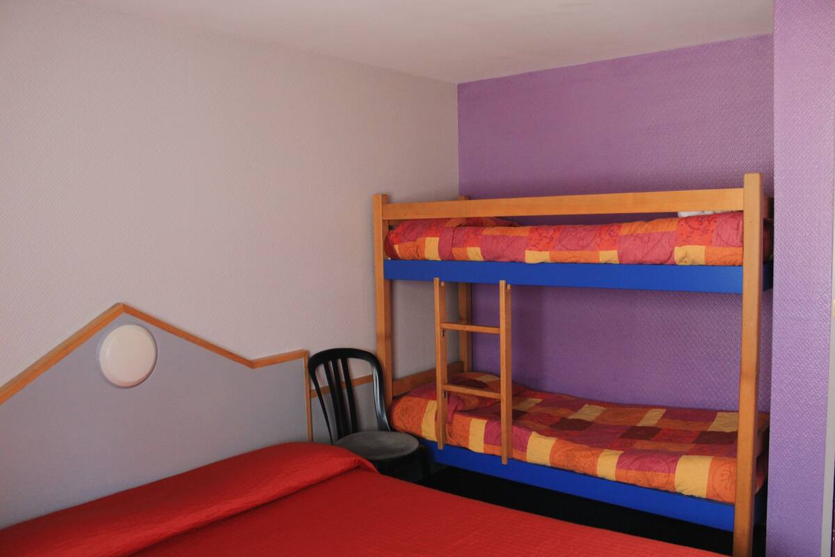 Ein Etagenbett mit einer Leiter, einem Stuhl und einer roten Bettdecke in einem Zimmer mit violetten Wänden.