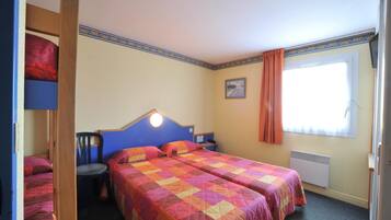 A bedroom with two beds, a chair, a nightstand, a window with curtains, and a radiator.