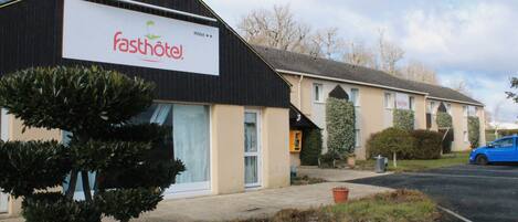 A building with a sign reading "fasthotel" and a blue car parked in front.