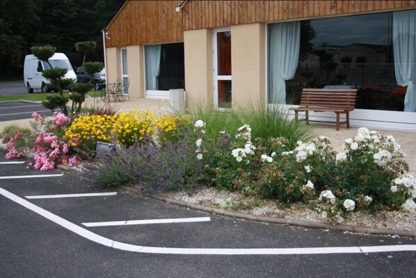 A building with a wooden facade, a bench, and a flower bed with various flowers. - Fasthotel Vendôme (Saint-Ouen)