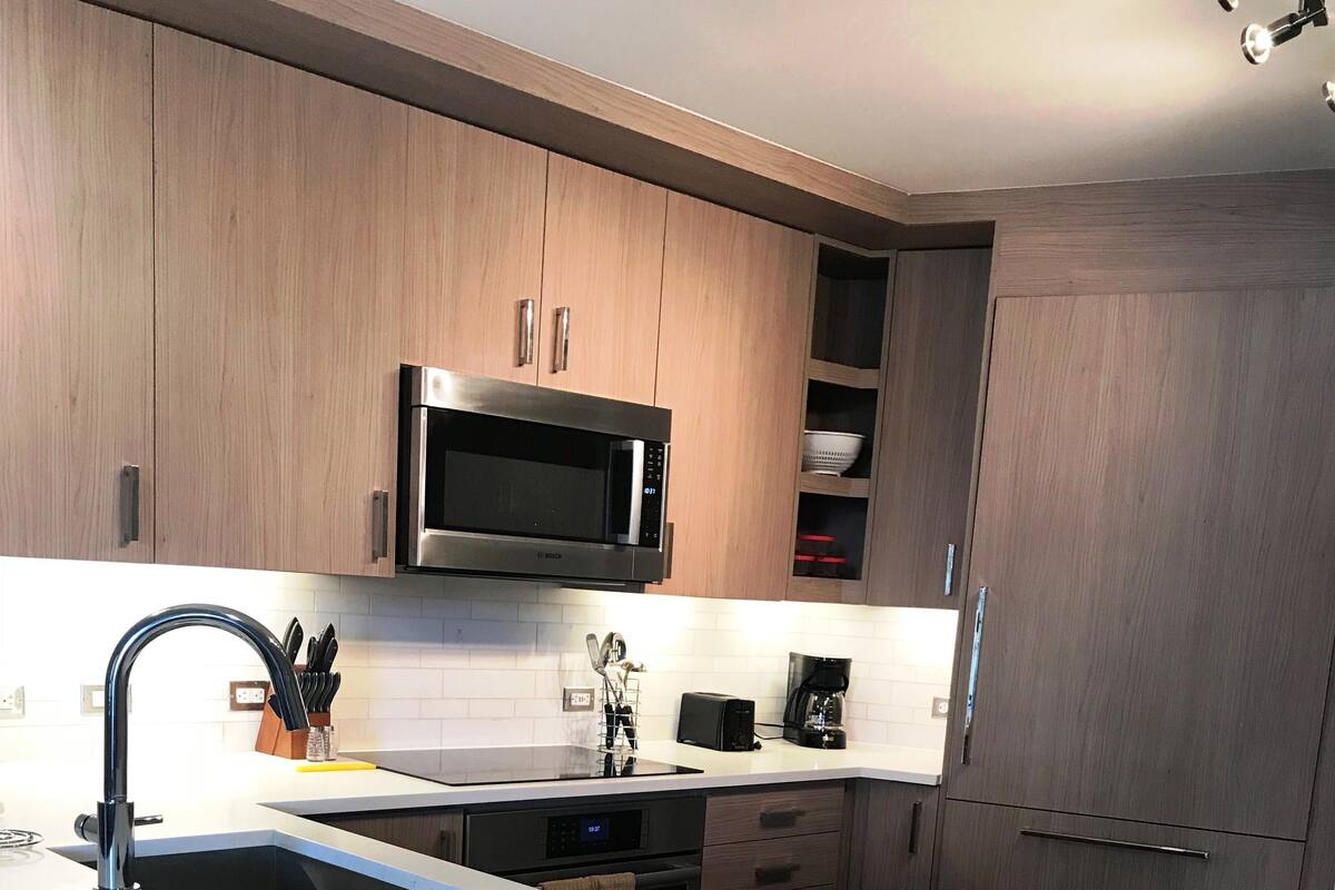 Une cuisine moderne dotée d’un îlot central, d’appareils électroménagers en acier inoxydable et de meubles de rangement en bois.