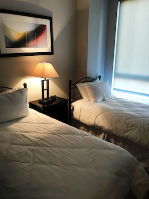 Ein Hotelzimmer mit zwei Betten, einem Nachttisch mit Lampe und einem gerahmten abstrakten Gemälde an der Wand.