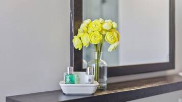 A bathroom vanity with a mirror, a vase of yellow flowers, and two bottles of lotion.