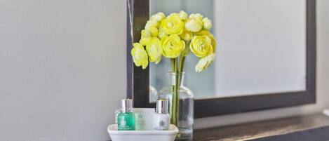 A bathroom vanity with a mirror, a vase of yellow flowers, and two bottles of lotion.