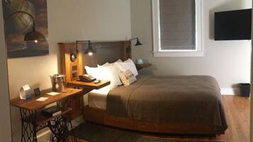 A bedroom with a bed, a desk with a sewing machine, a nightstand, and a wall-mounted TV.