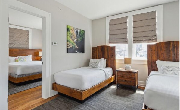 A hotel room with two beds, a nightstand, a painting, and a window with blinds. - Western Front Hotel (St. Paul)