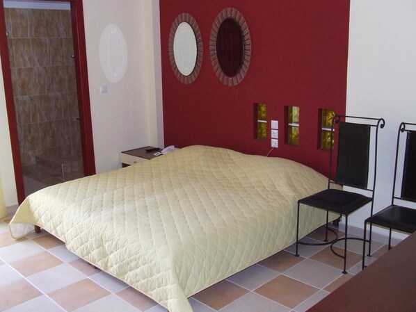Un dormitorio con una cama grande, una mesita de noche pequeña, una silla y una zona de ducha.