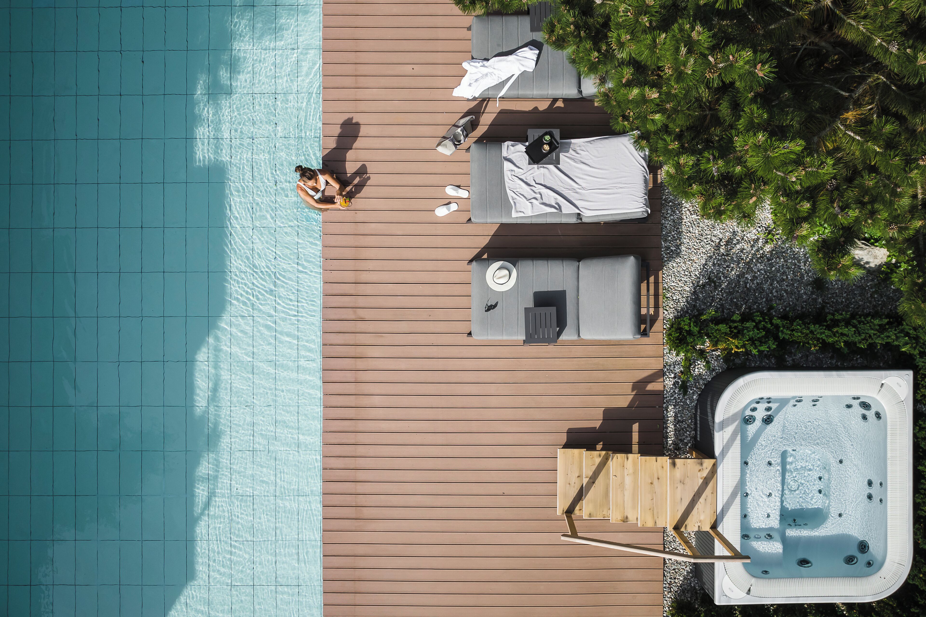 An aerial view of a poolside area with a hot tub, lounge chairs, and a wooden deck.
