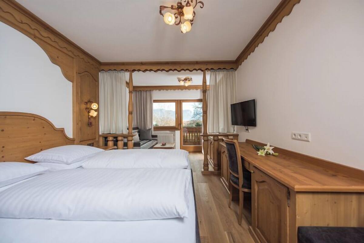 A room with two beds, a wooden desk, a television, and a view of the outdoors.