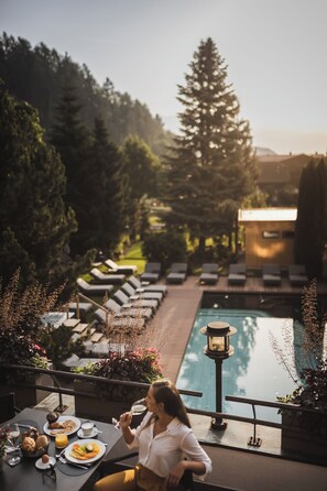 Un área de comedor junto a la piscina con tumbonas, una piscina y vistas del bosque circundante.