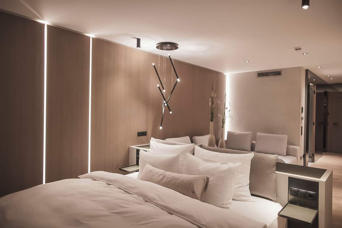 A modern bedroom with a large bed, bedside tables, a decorative light fixture, and a vase with plants.