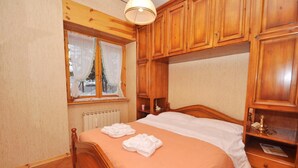A wooden-framed bedroom with a bed, a window with a view, and built-in wooden cabinets. - Amami Viaggi - Casa del Sannio (Roccaraso)