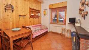 A cozy room with a wooden dining table, a sofa, a TV, and a window with a curtain. - Amami Viaggi - Casa del Sannio (Roccaraso)