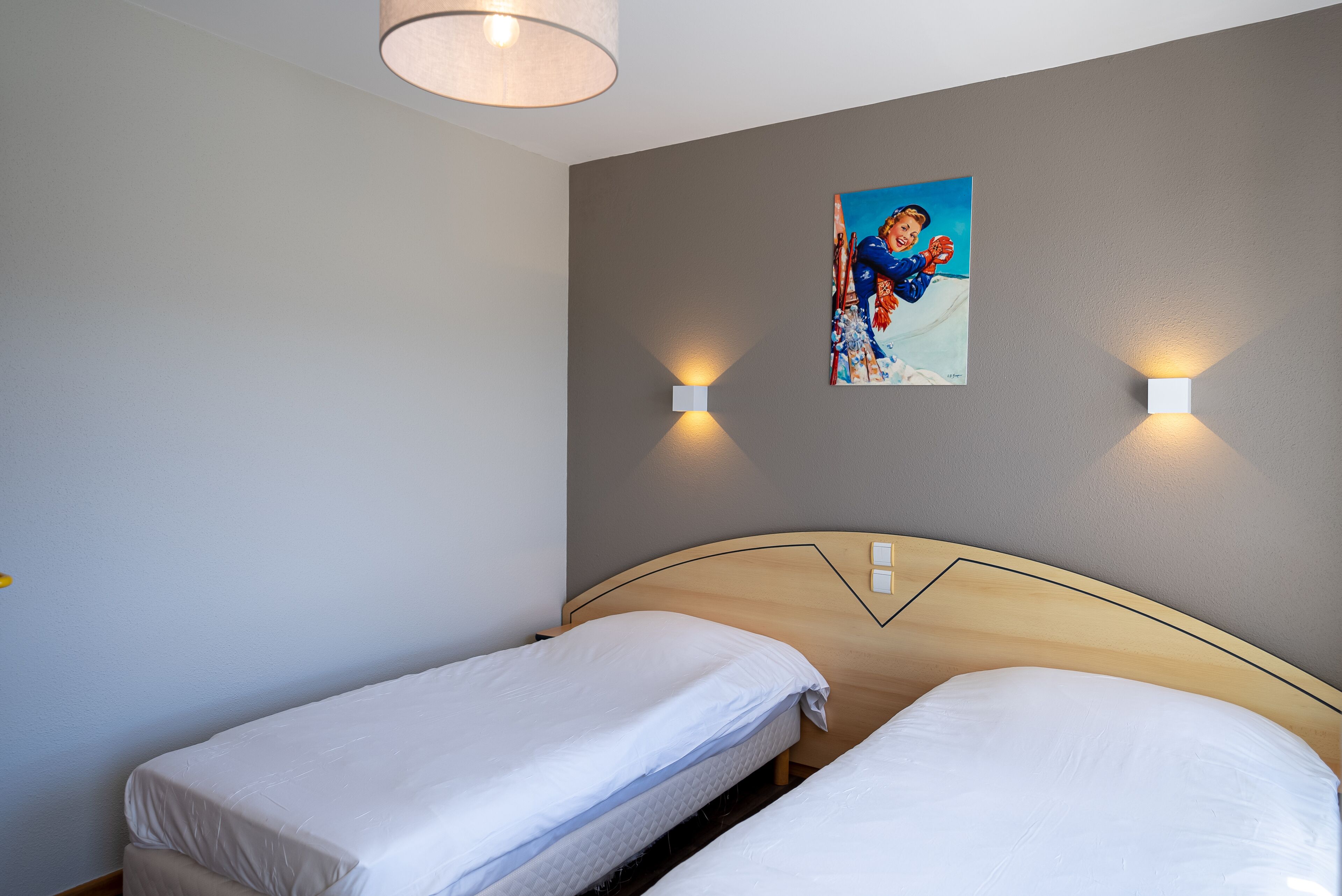 Ein Hotelzimmer mit zwei Einzelbetten, einem Holzkopfteil, einem Gemälde an der Wand und zwei Wandleuchten.