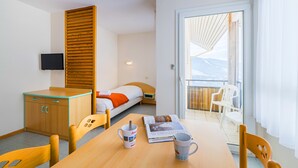 Habitación de hotel con cama, escritorio, silla, mesa, televisor y balcón con sillas.