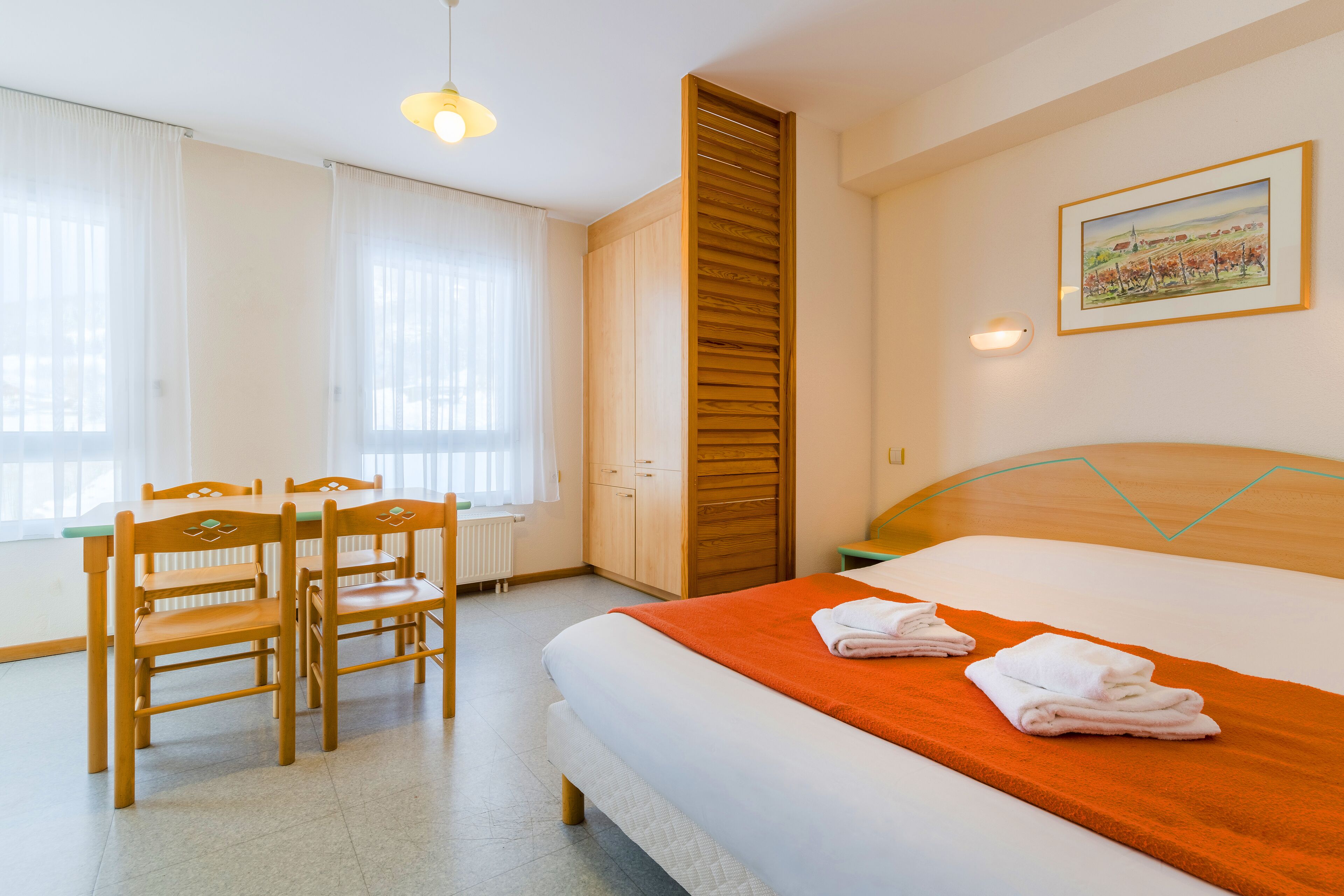 Et hotelværelse med en seng, et skrivebord med stole, en radiator og et billede på væggen.