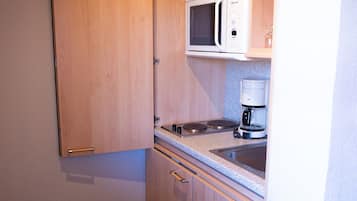 Een kleine keuken met houten kastjes, een magnetron en een koffiezetapparaat.