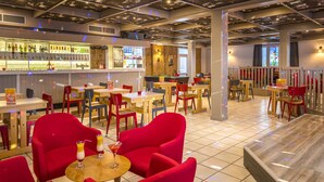 Zona de bar con diversas opciones de asientos, incluyendo sillas y mesas rojas, una barra con diferentes botellas y un panel de madera.