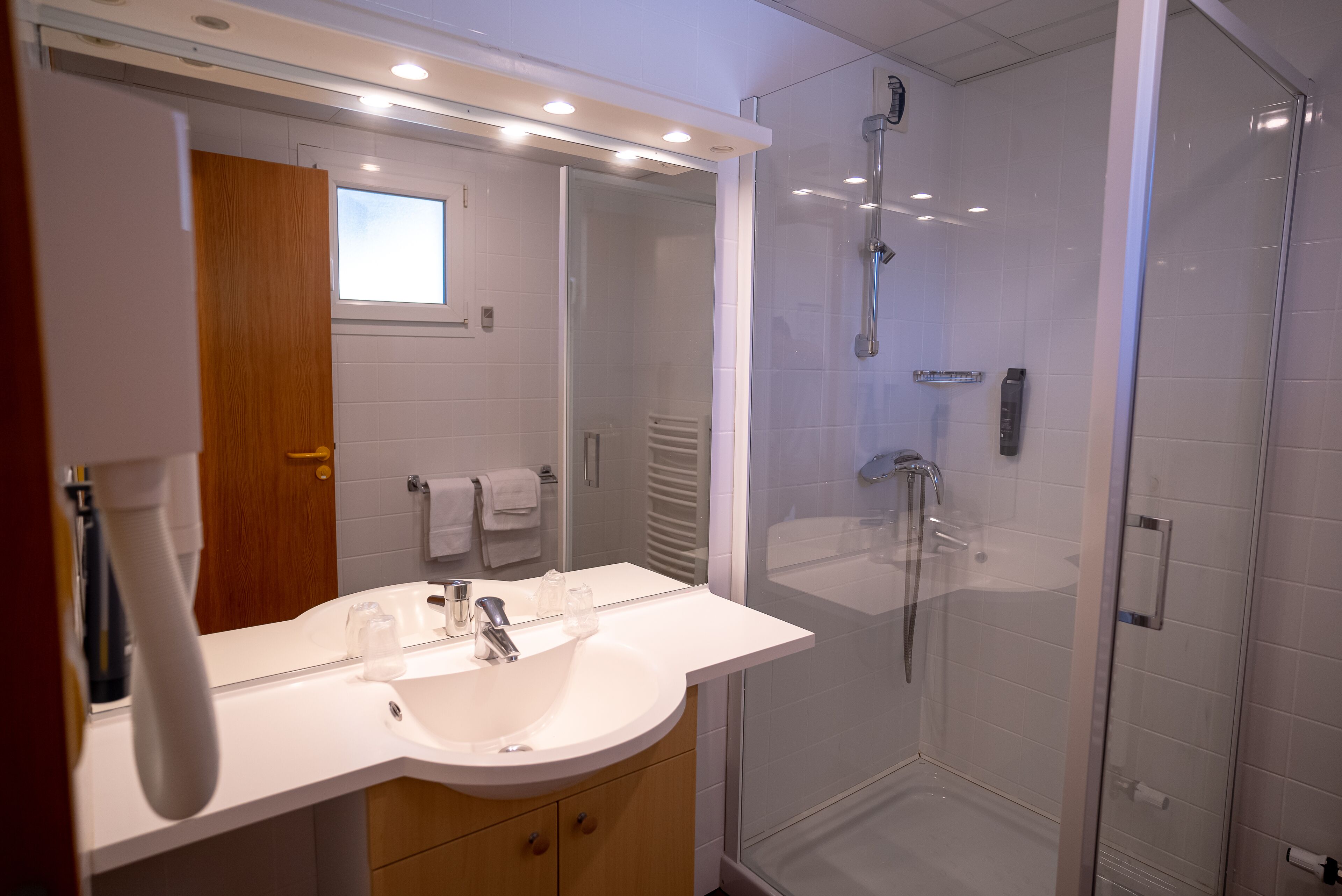 Une salle de bain moderne avec un lavabo blanc, un miroir et une douche à parois de verre.