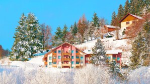 Un edificio de varios pisos con fachada roja y amarilla, rodeado de árboles cubiertos de nieve y un cielo azul despejado.