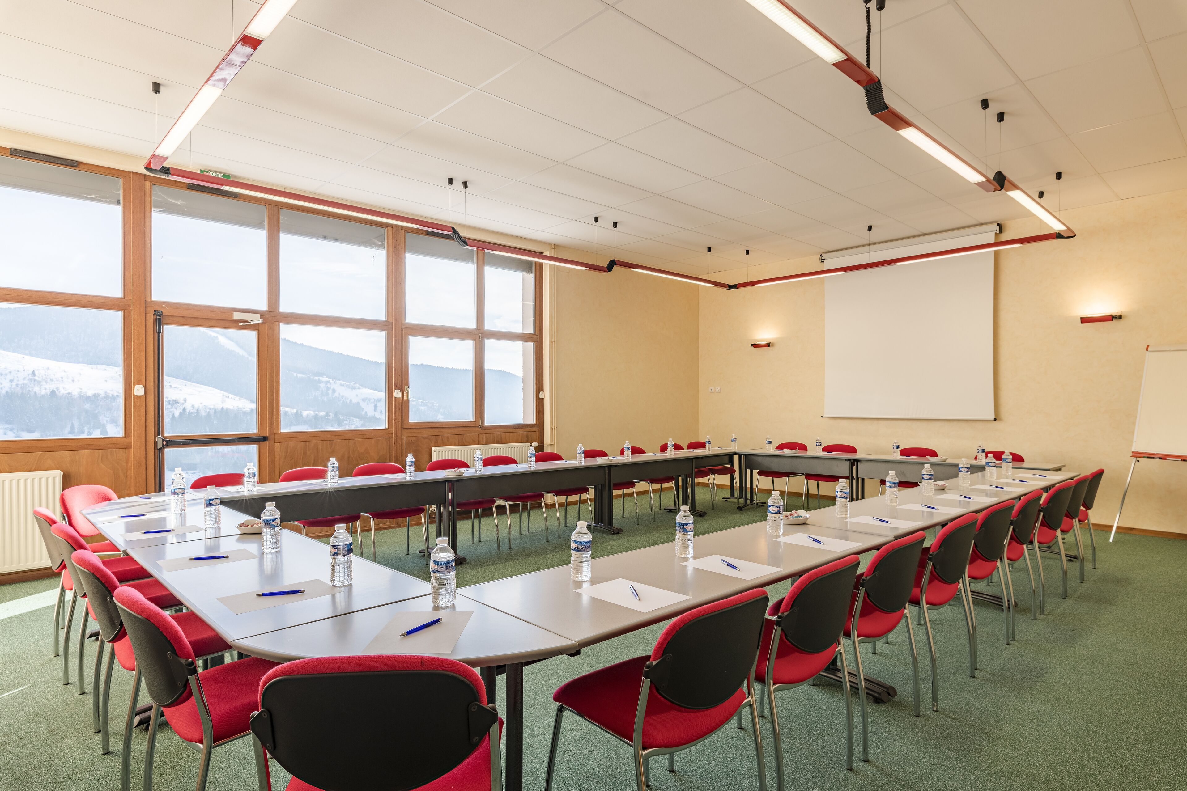 A conference room with a long table, red chairs, water bottles, and a whiteboard.