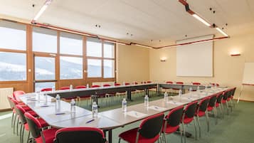 Een vergaderzaal met een lange tafel, rode stoelen, waterflesjes en een whiteboard.