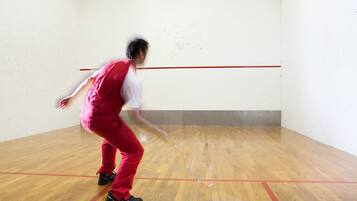 Eine Person spielt Squash in einem Raum mit Holzboden und roten Linien, die das Spielfeld markieren.
