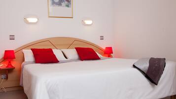 Een net opgemaakt bed met wit en rood beddengoed, twee bedlampen en een lijst met een kunstwerk aan de muur.