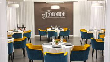 Ein Restaurant-Interieur mit gedeckten Tischen, blaue und gelbe Stühle, und ein Schild mit der Aufschrift "LA ROTONDE Restaurant".