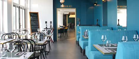 Un restaurante con mesas y asientos tipo banqueta, algunos con copas de vino.