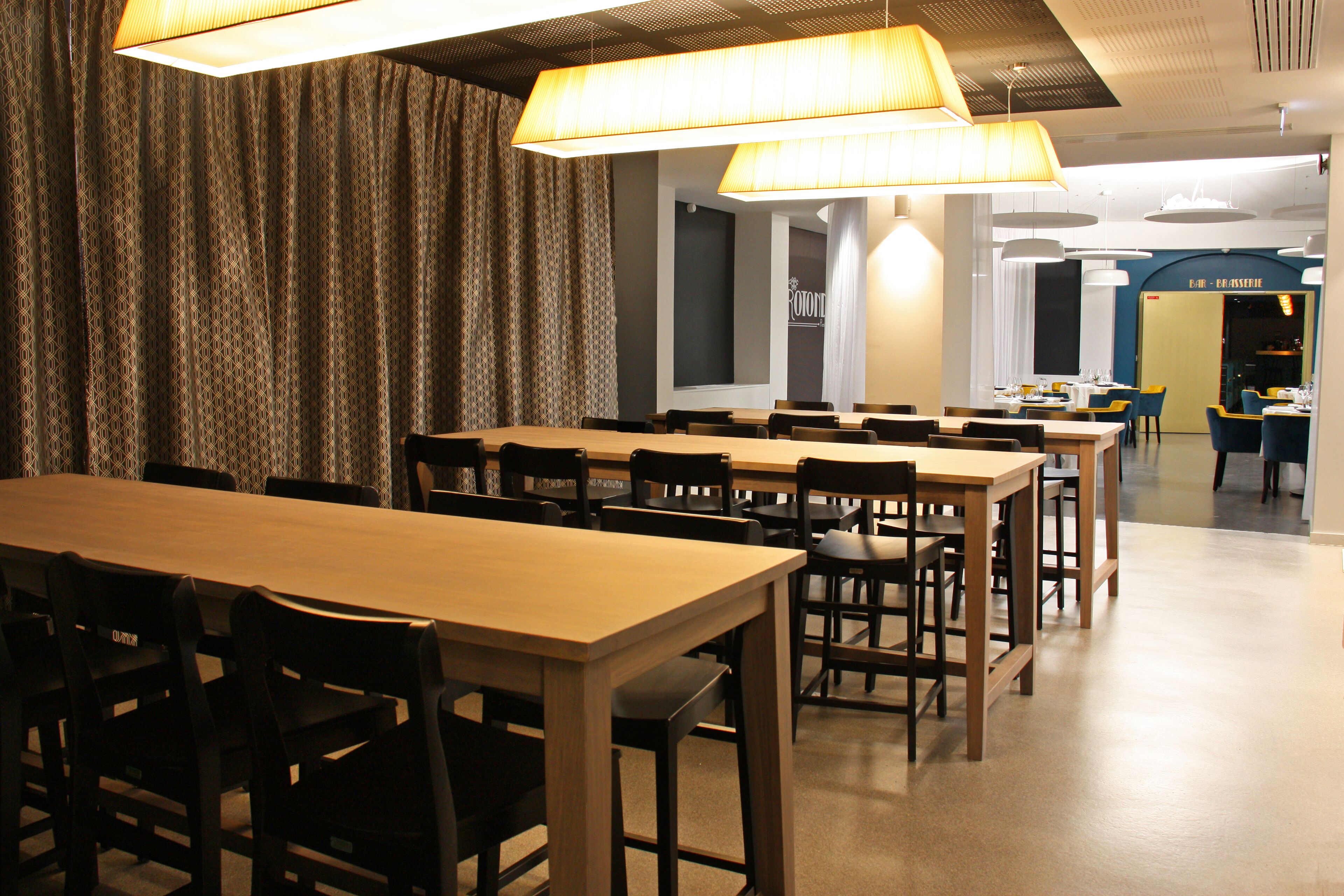 Un espace repas comprenant plusieurs tables et chaises, un fond constitué d’un rideau à motifs et un design moderne au niveau du plafond.