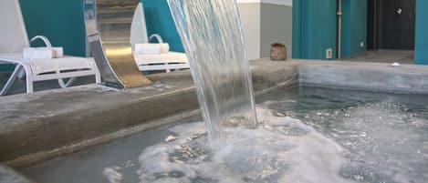 A spa area with a water feature and lounge chairs.