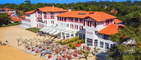 Un hotel con varios edificios de techo rojo, un área de estar cubierta al aire libre y una playa en primer plano.