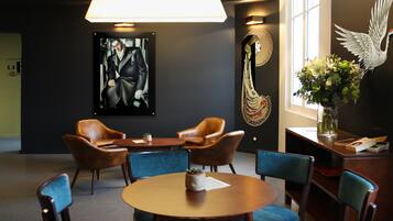 A conference room with a round table, four chairs, a large painting, a decorative wall hanging, and a vase with flowers.