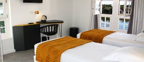 Habitación de hotel con dos camas, un escritorio, una silla y un televisor en la pared.